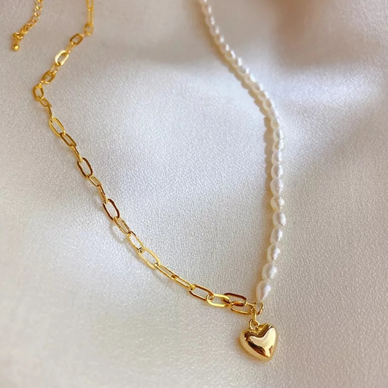 Gold necklace with a heart pendant on a light pink background