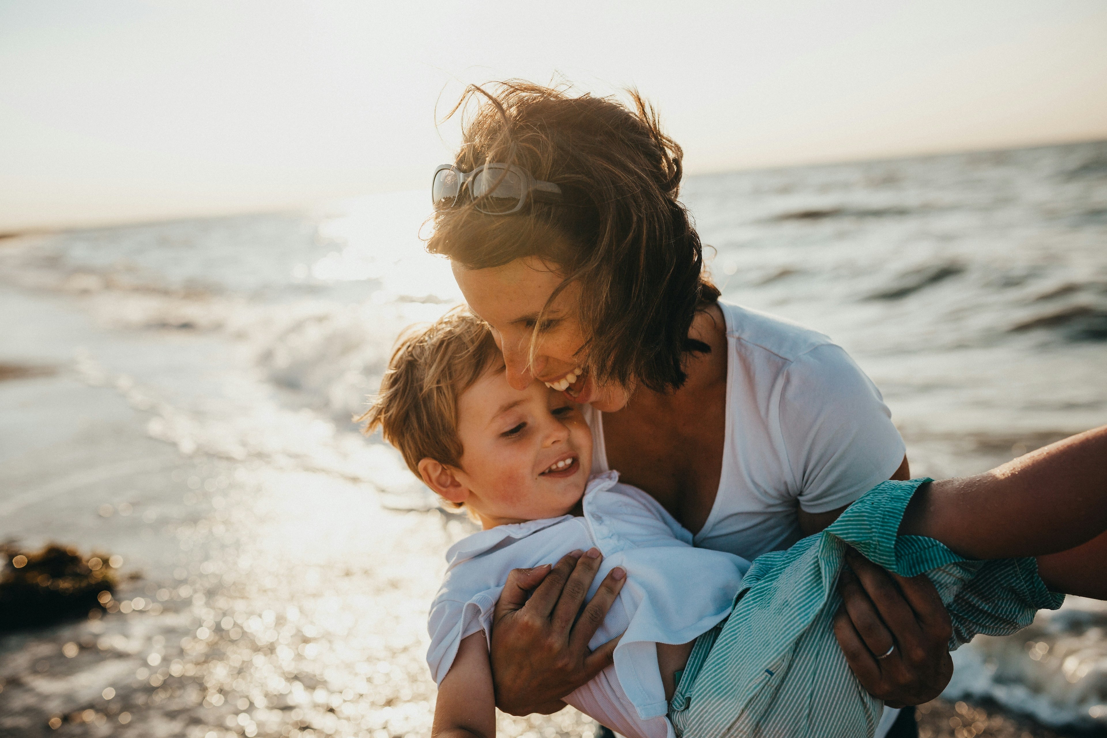 Women holding her young son beside the beach, both are very happy and laughing.